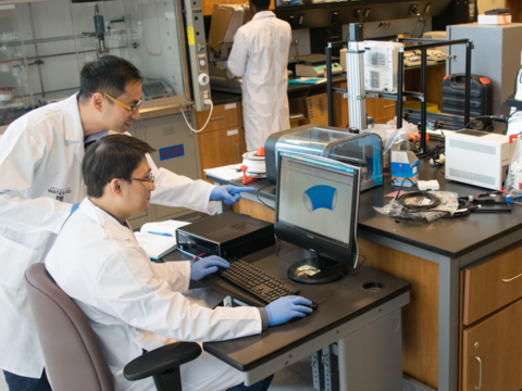 Two people working on laptop wearing white coats. 