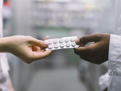 A hand passing a blister pack of medications to another hand