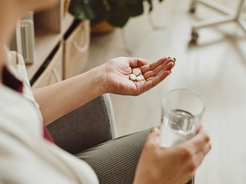 A hand holding a glass of water and pills