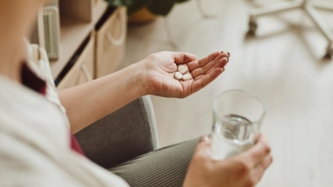 A person holding a glass of water and pills.