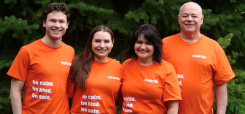 The Tennant family (four people) wearing orange shirts in front of some trees