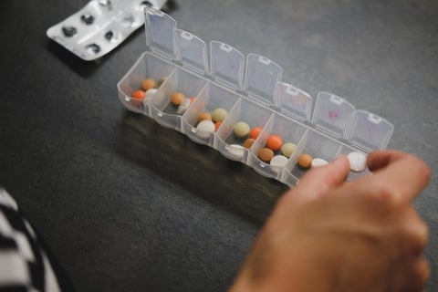 A hand placing pills in a pill box.