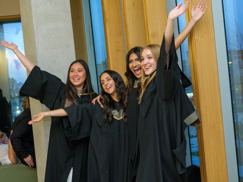 Students smiling in convocation robes with their hands up