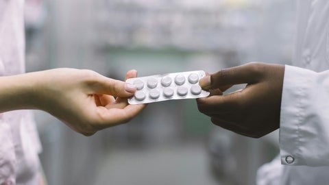 A hand passing a blister pack of medications to another hand