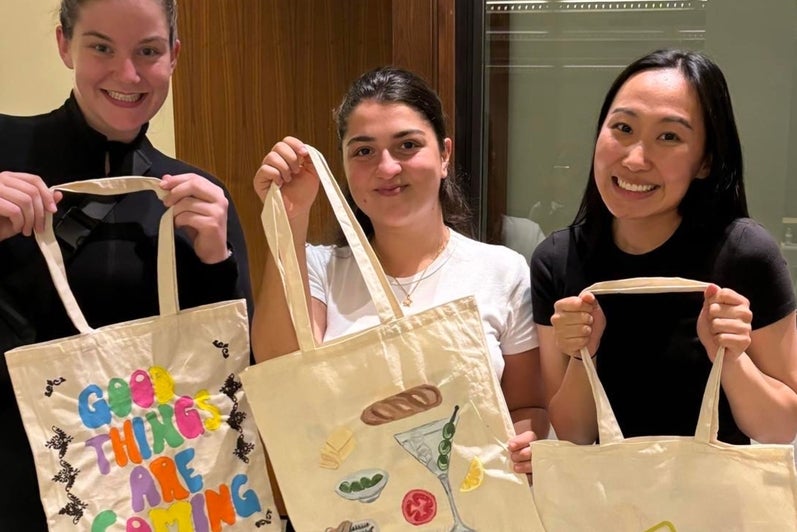 Three students holding up tote bags