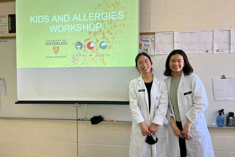 Two pharmacy students smile in front of projected slideshow