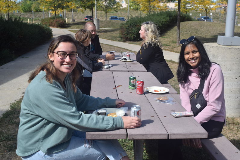 Two students sitting at picnic table smiling 