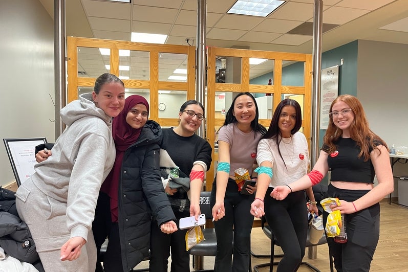 Students smiling holding their arms out to show their blood donation