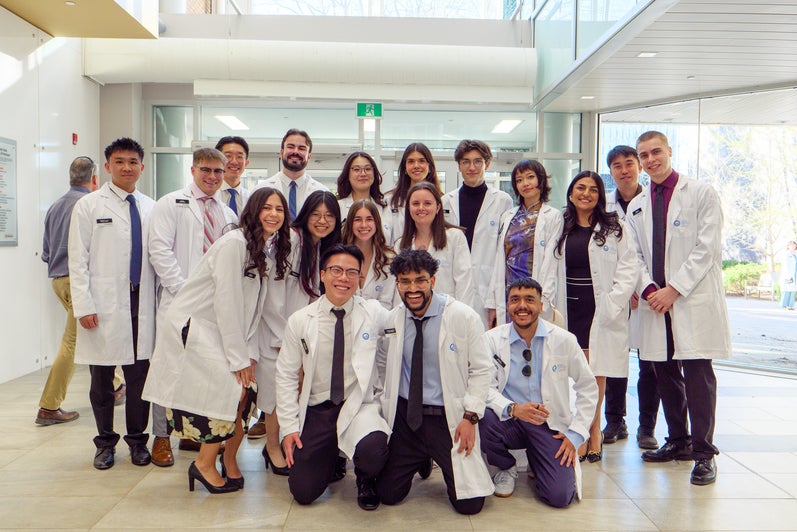 Small group of pharmacy students in white coats posing together in a bright campus lobby.
