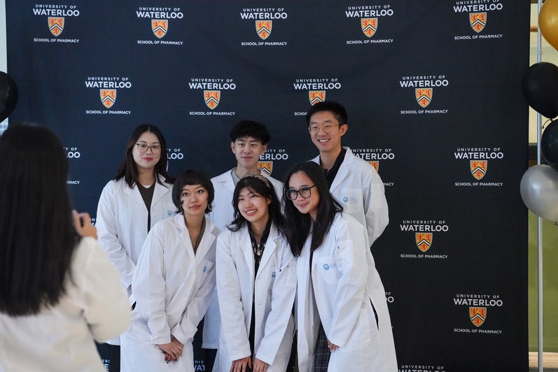 Students smiling and posing in front of a backdrop in lab coats