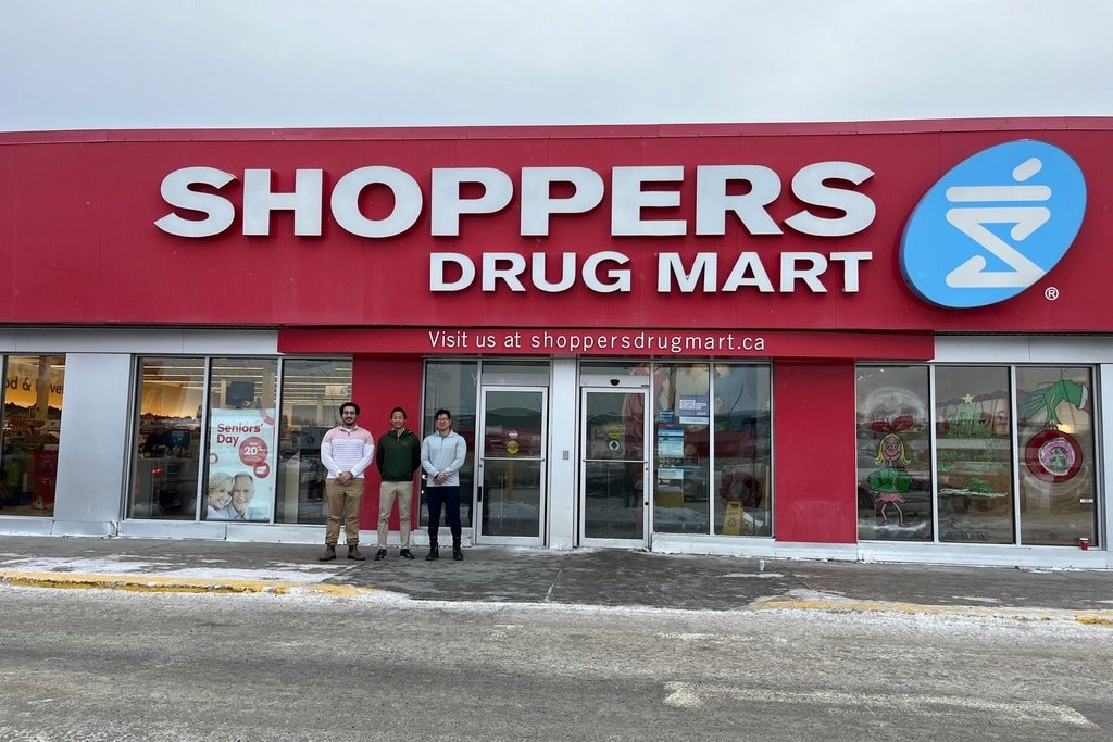 Three people standing outside of a Shoppers Drug Mart store