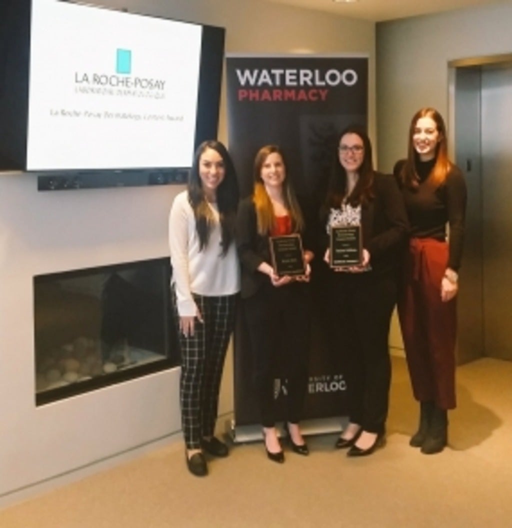 Women standing next to a banner holding awards