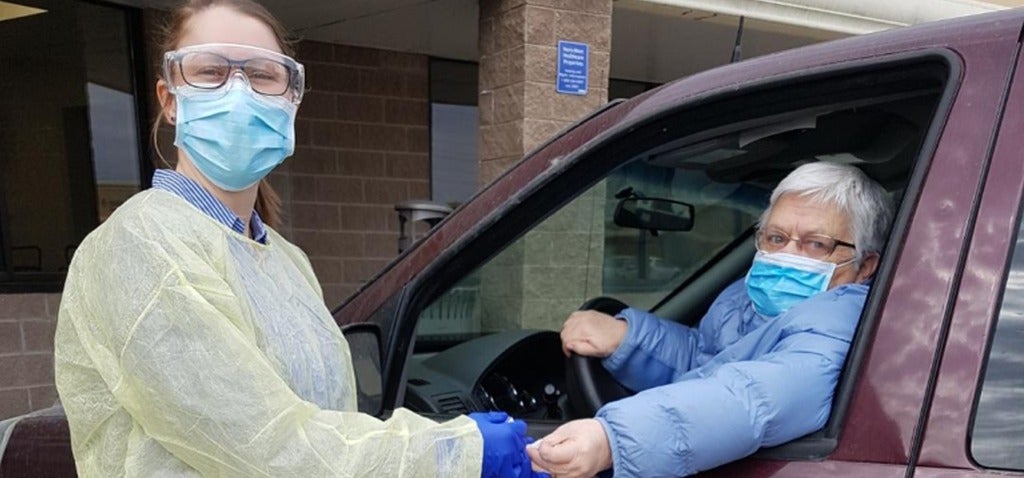 Dani Thomas wearing protective equipment and pricking a patient's finger while the patient sits in her vehicle