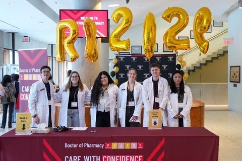 Students smiling standing behind a welcome table