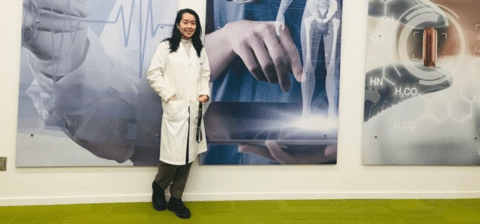 Amy in a lab coat standing in front of a wall