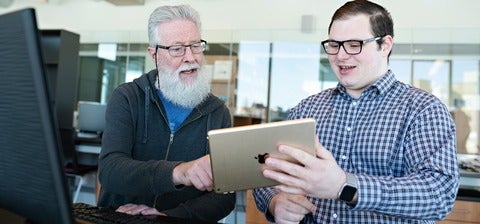 Colin holding a tablet and gesturing to it while an older adult with glasses watches