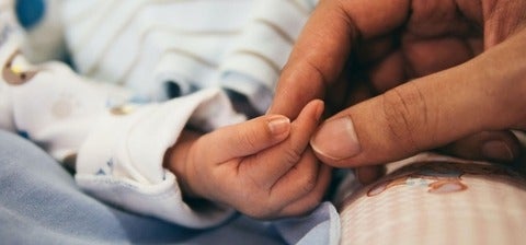 An adult hand holding a babies hand