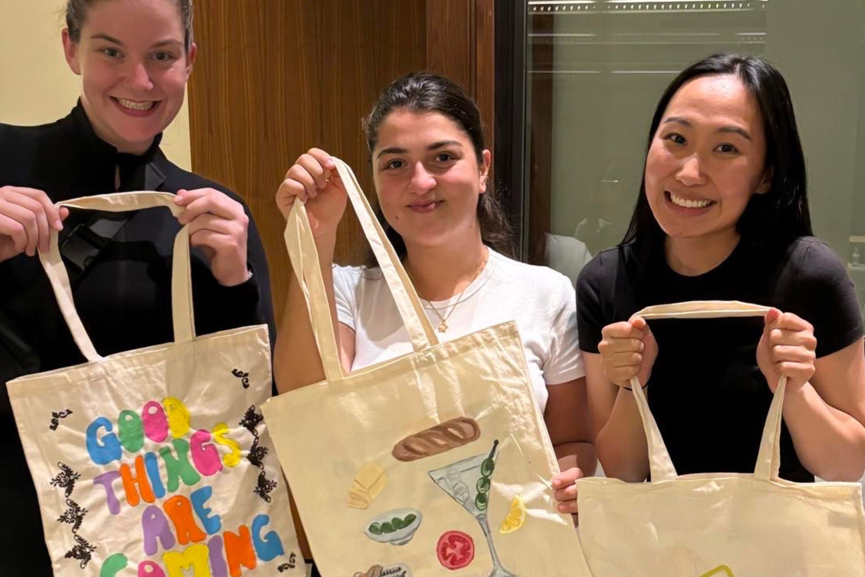 Three students holding up tote bags