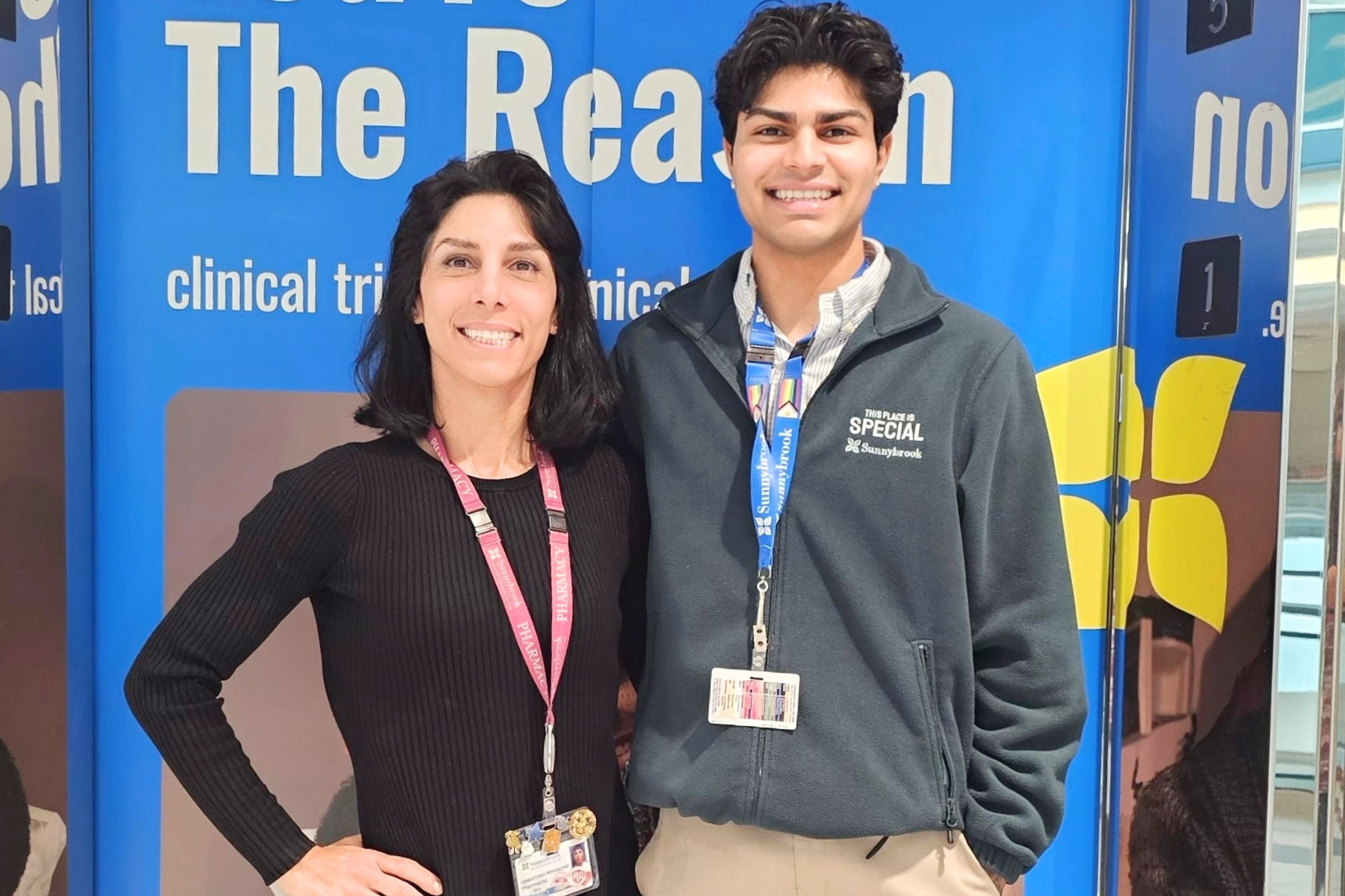 Christine Peragine and Armaan Mahajan smiling in front of a banner 