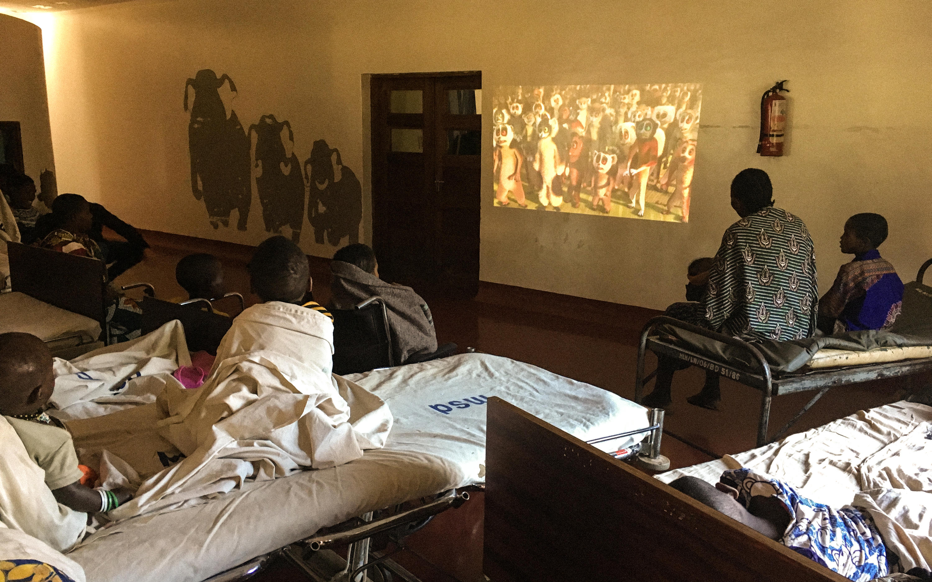 Children watching a movie projected on the wall in the hospital