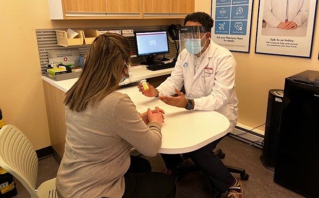 Mohamed wearing a lab coat and PPE as he consults with a patient in the pharmacy