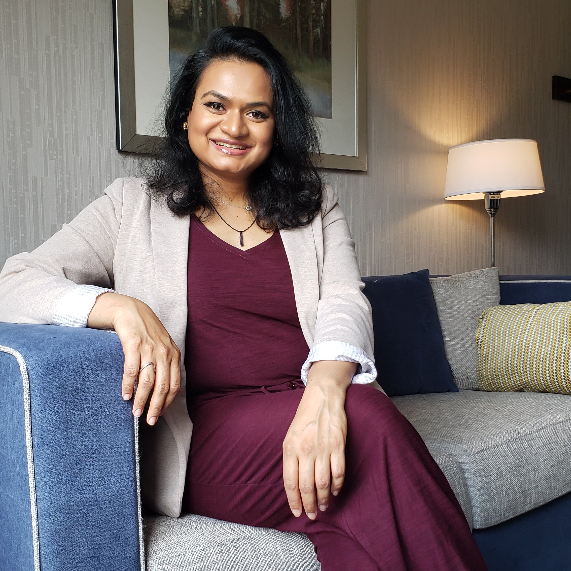 Aska Patel sitting resting her arm on couch smiling.