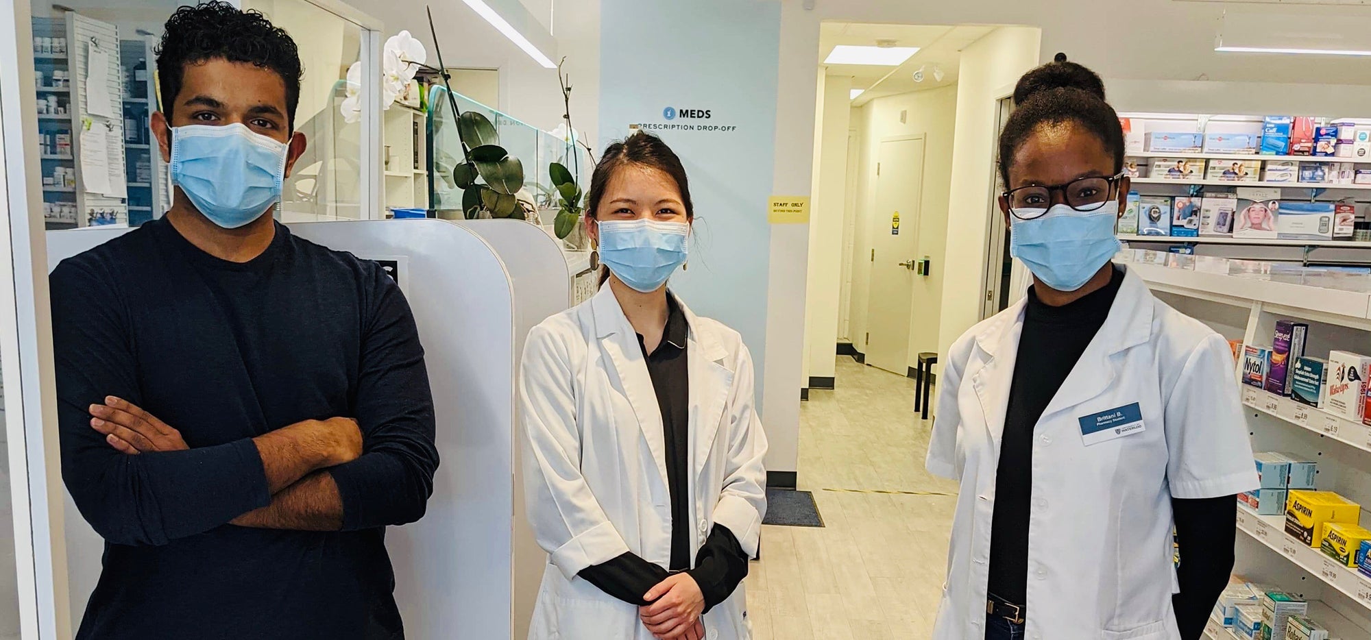 Three pharmacists wearing masks and standing in the pharmacy