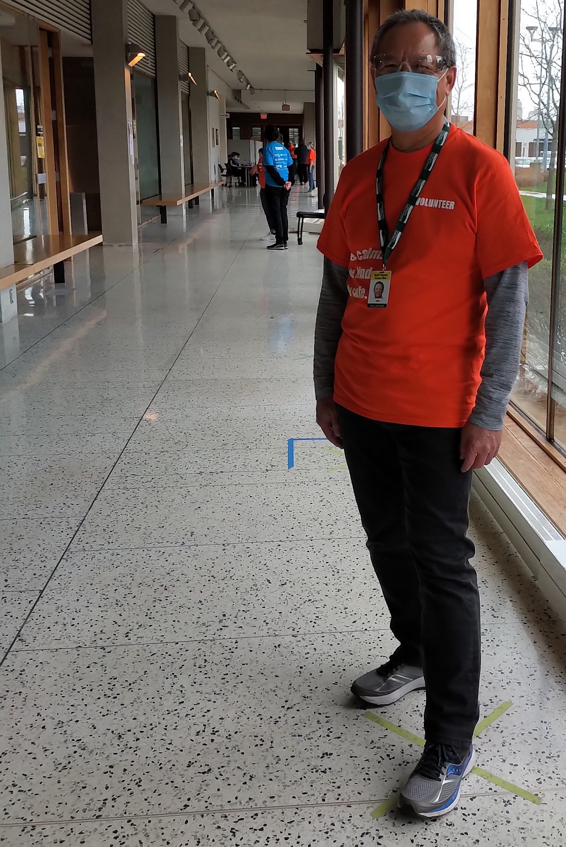 Tim wearing an orange volunteer shirt and PPE standing in the clinic