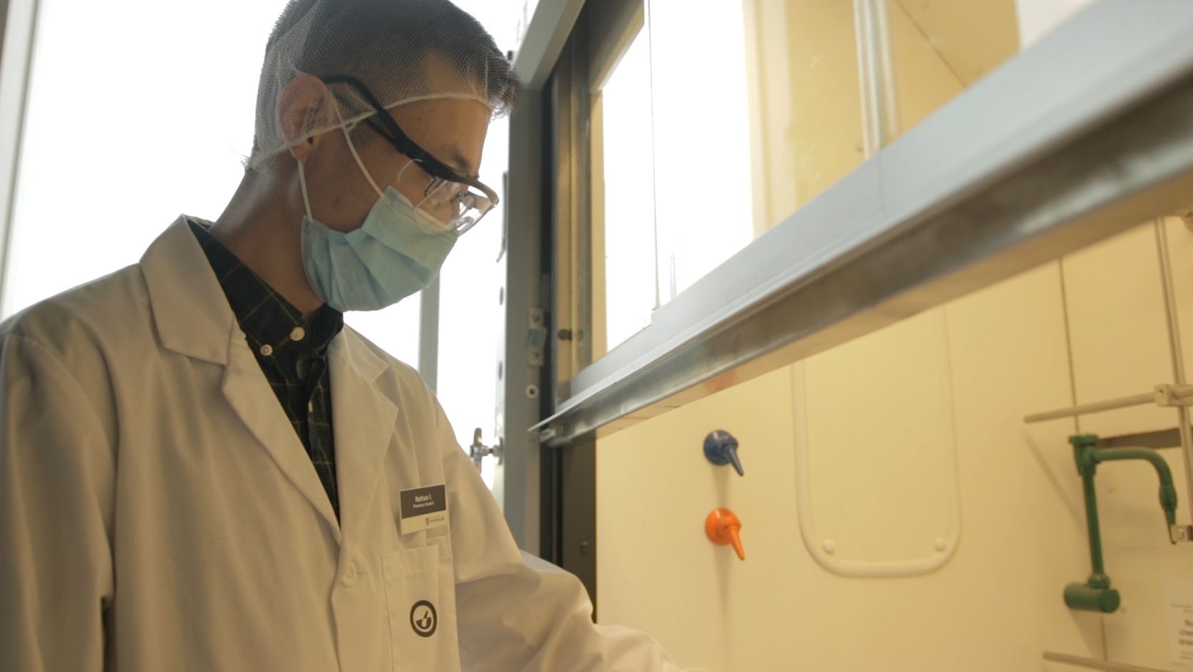A student with a lab coat and mask working at fume hood