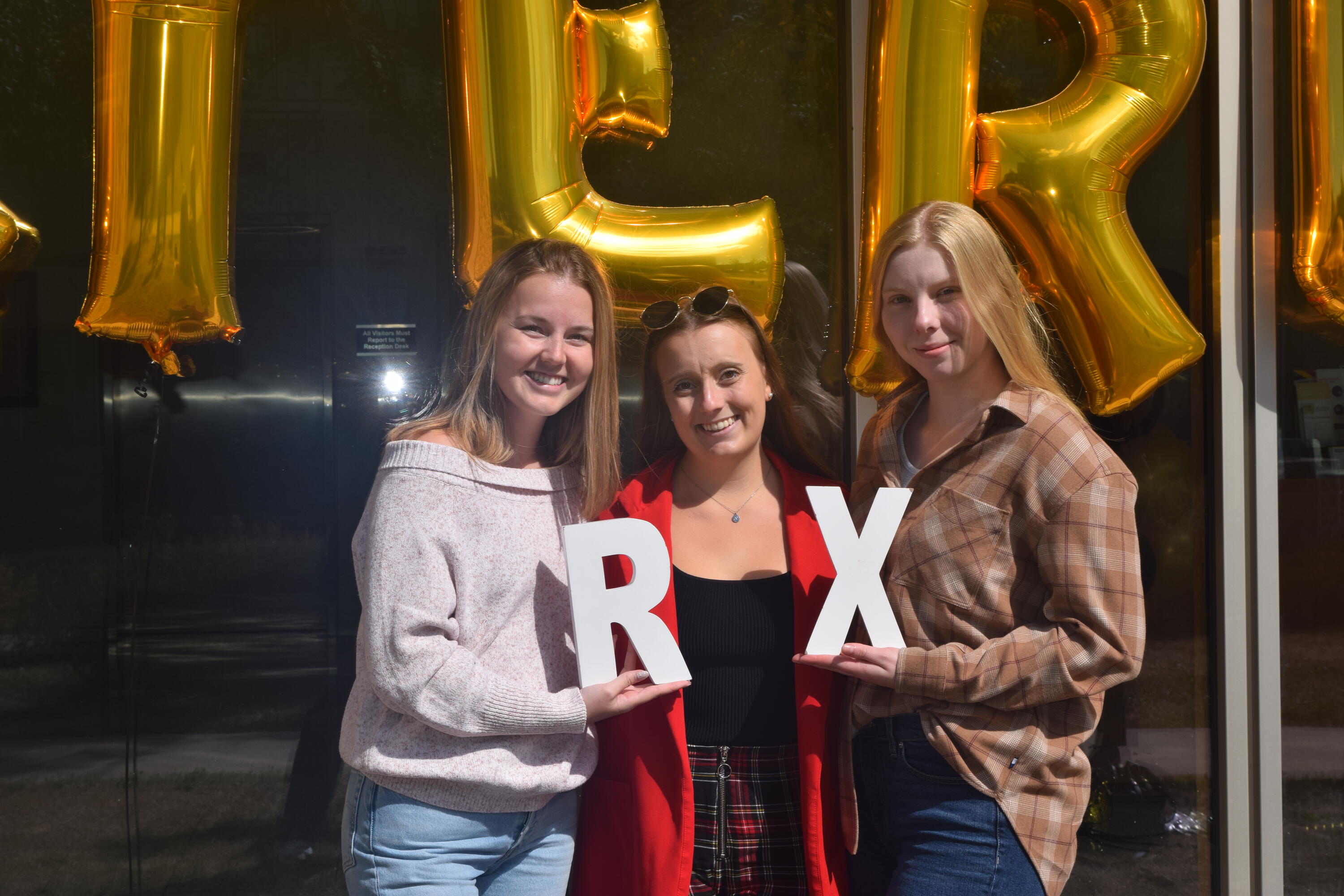 Three women smiling while holding up the letters "Rx" 