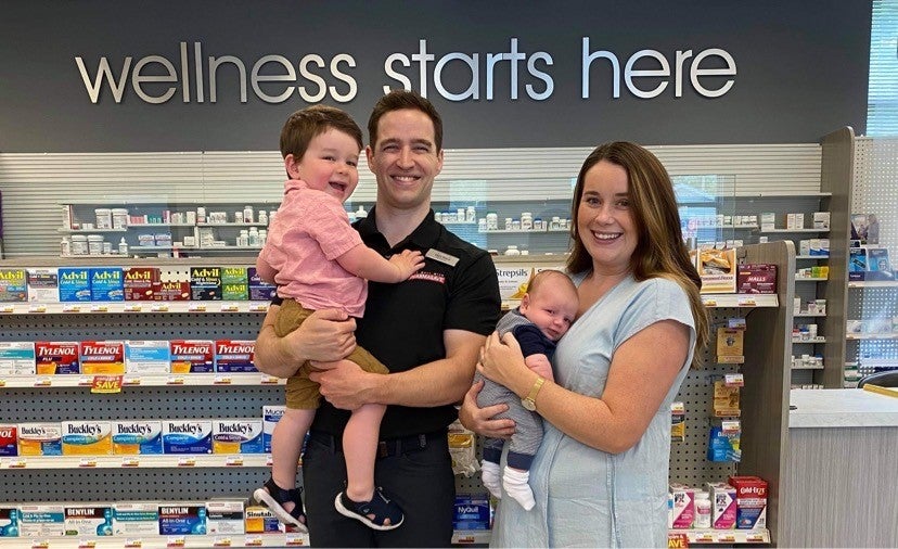 Evan Steed and his wife and children standing in the pharmacy and smiling