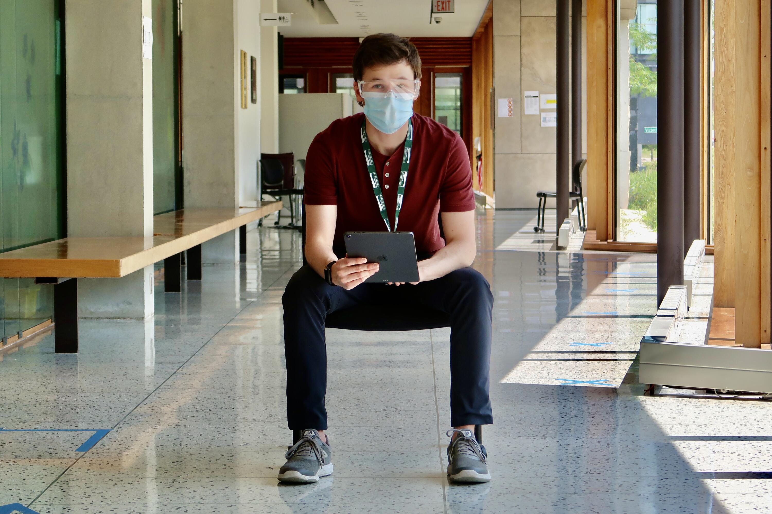 Ryan wearing PPE in a hallway with a tablet