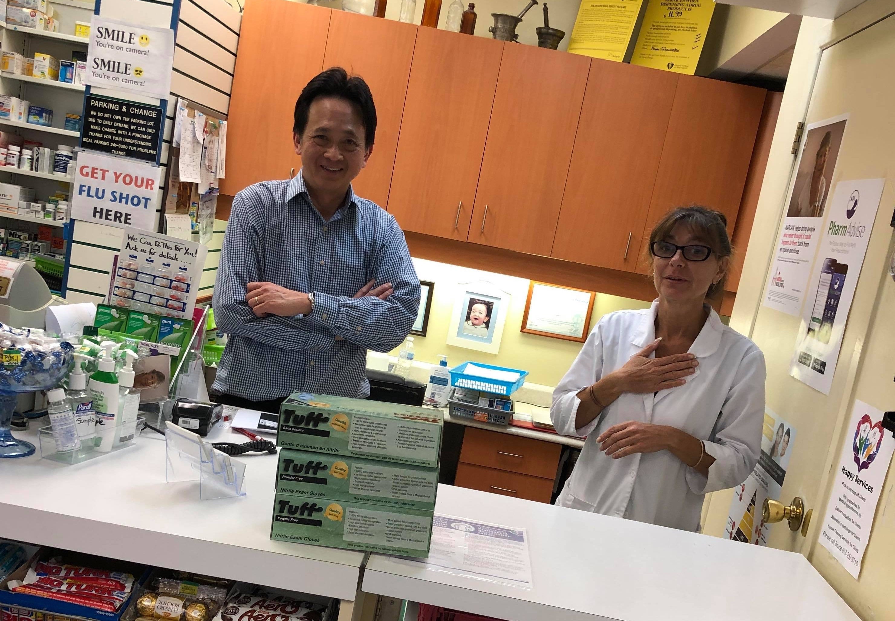 A man and woman standing behind a pharmacy counter smiling as they recieve a donation