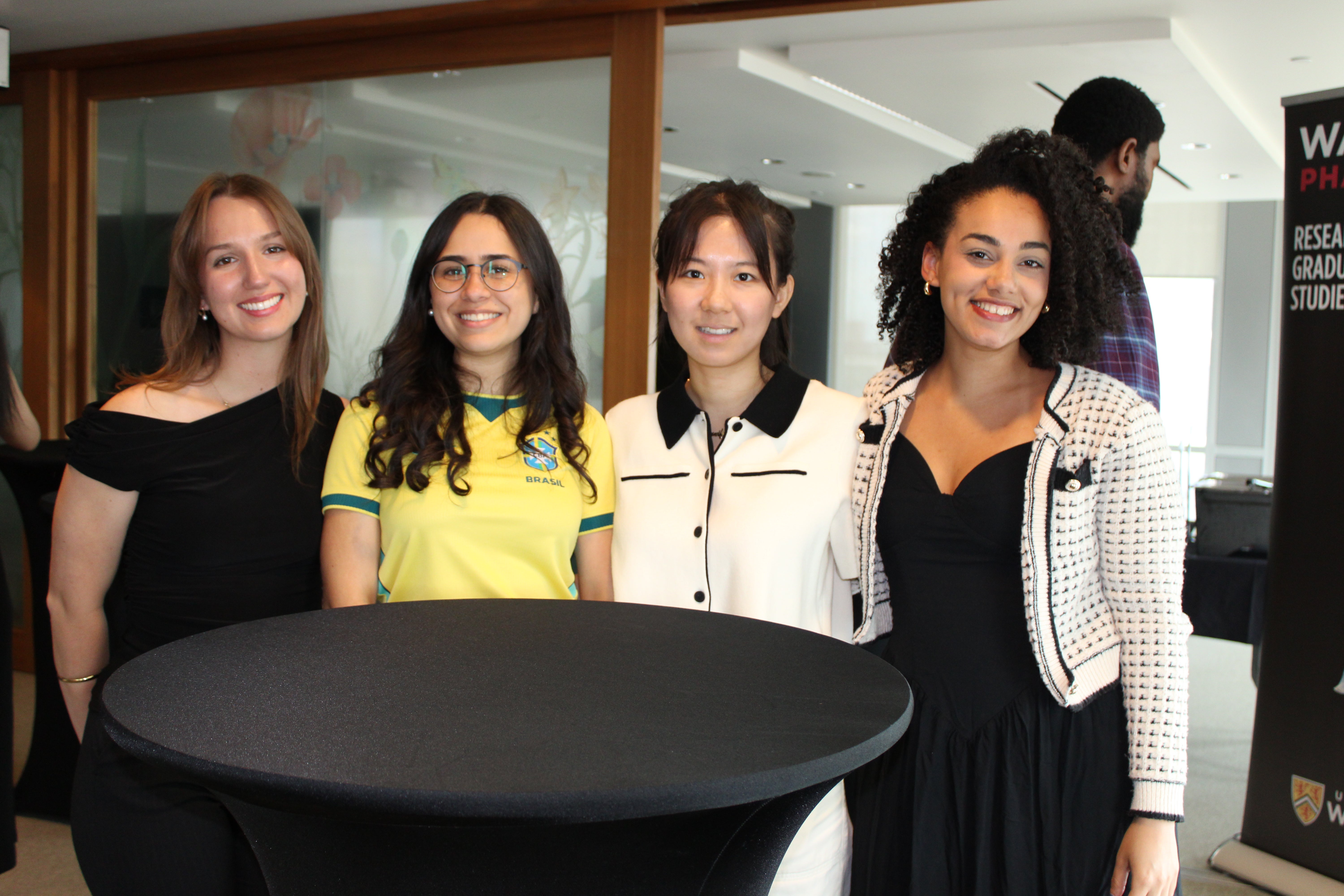 Four people standing around a tall table in a campus lounge, with a University of Waterloo banner in the background.