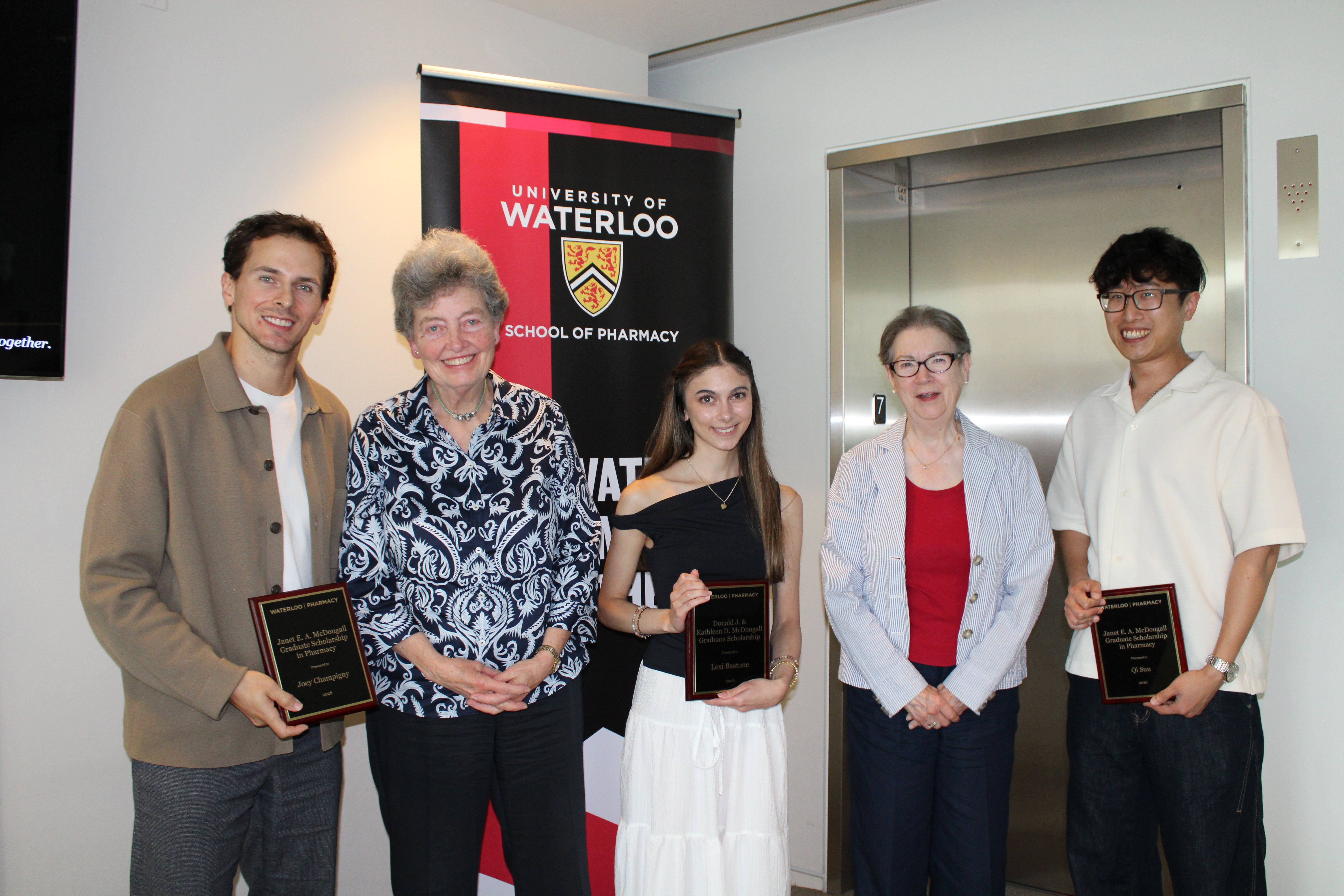 Five people holding award plaques stand beside donors in front of a University of Waterloo Pharmacy banner.