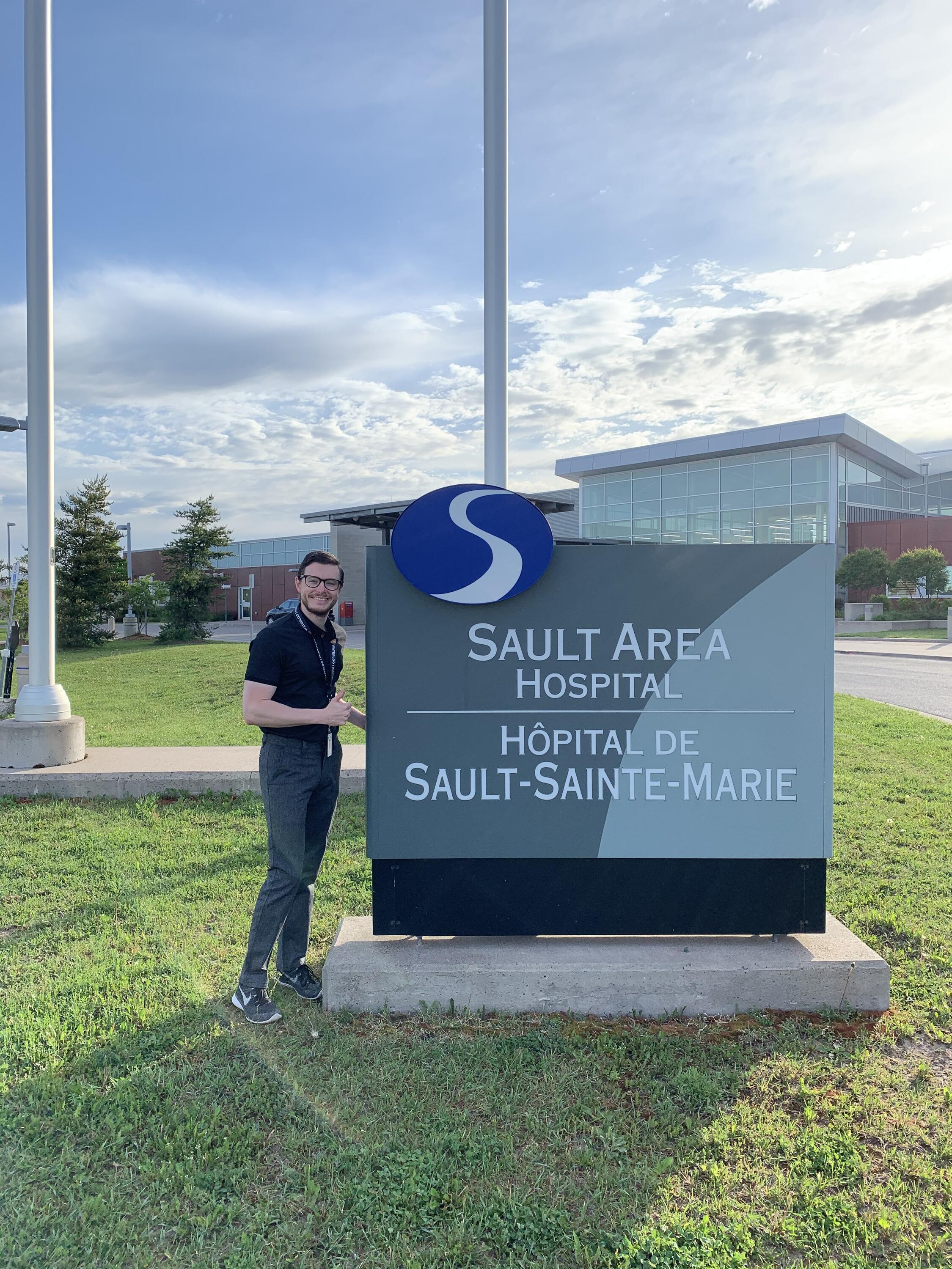 Ryan standing by a sign in front of the Sault Area Hospital