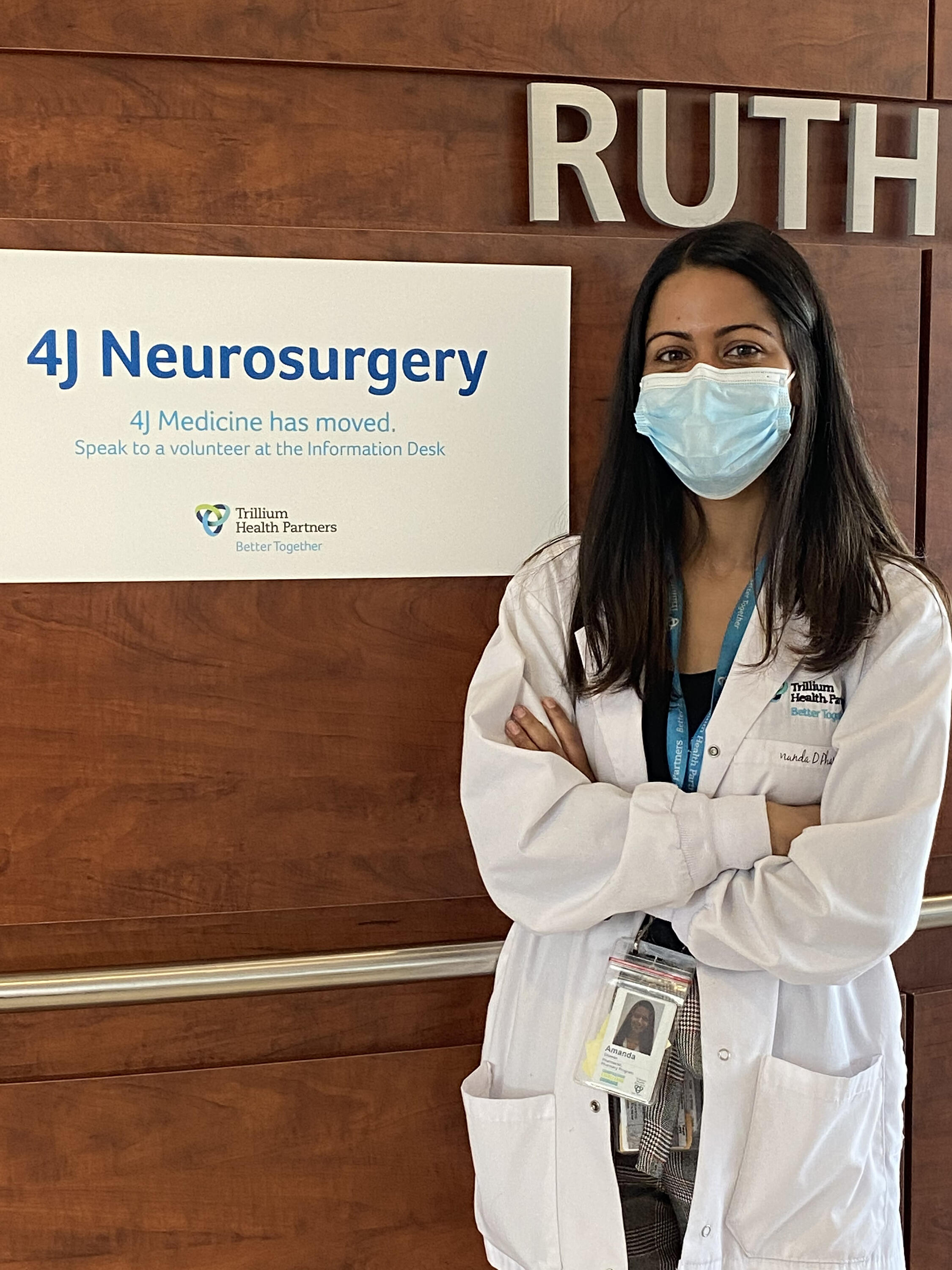 Amanda Dhawan wearing a mask and lab coat next to a neursurgery sign