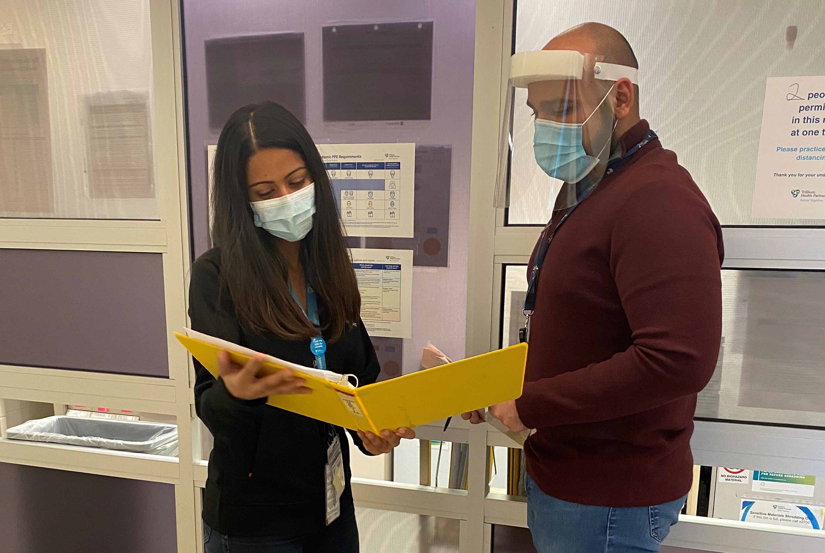 Amanda and a colleague wearing masks and studying a binder