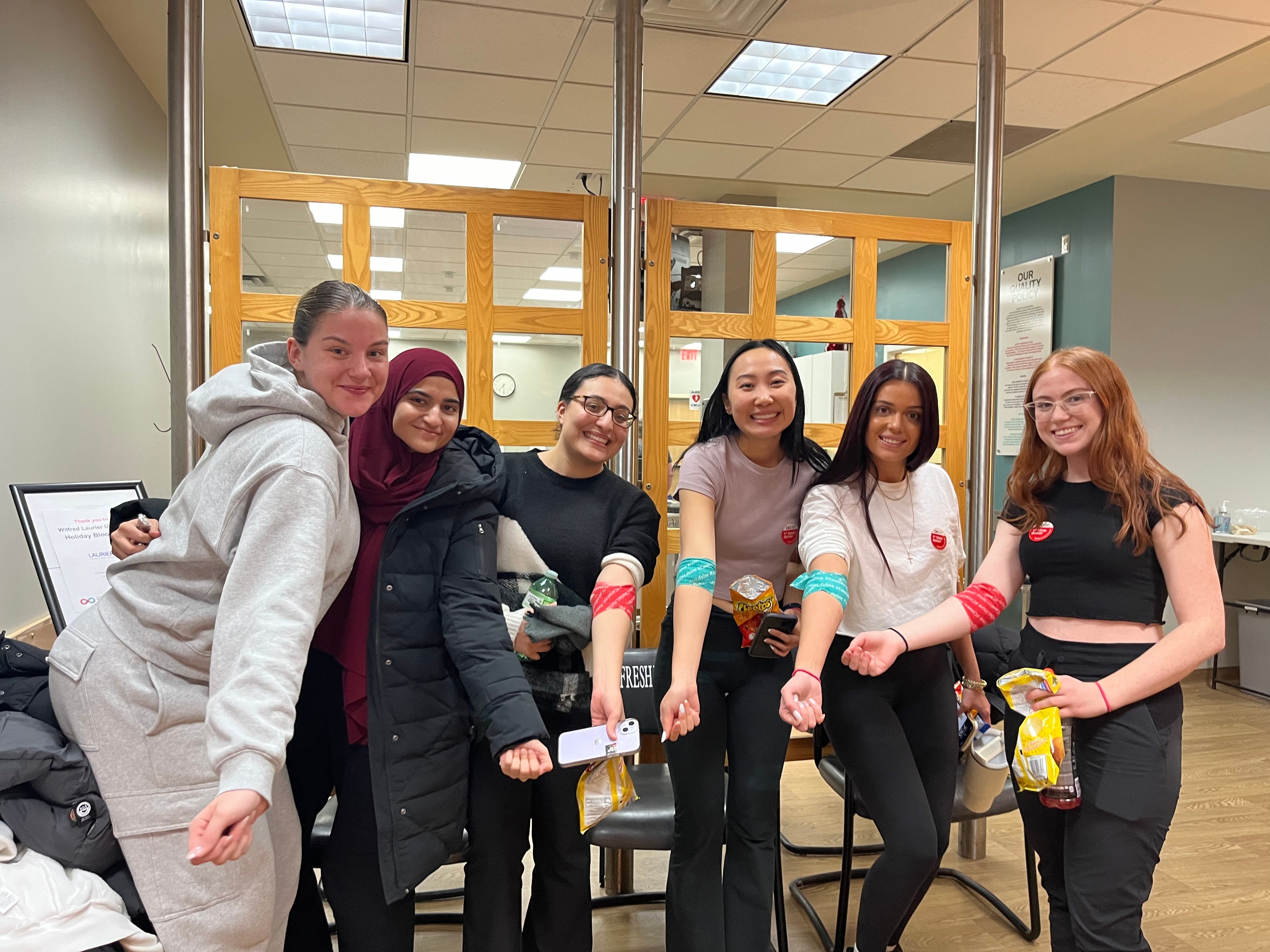 Students smiling holding their arms out to show their blood donation