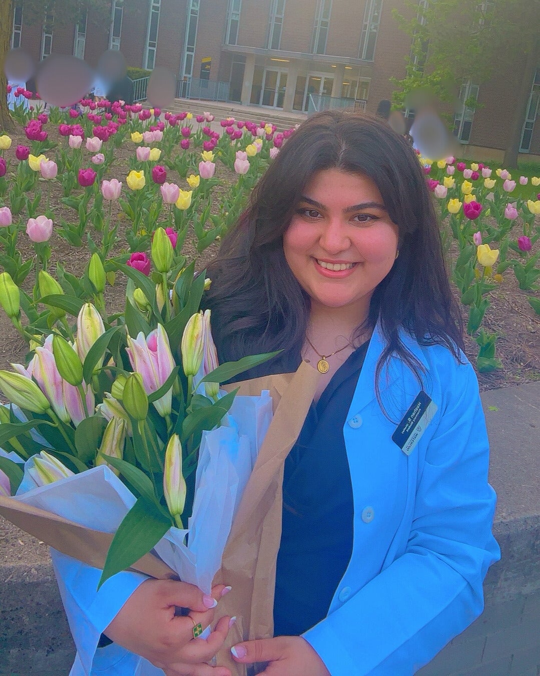 Headshot of Recruitment Director, Rojan Shaeri, standing in front of a garden holding a bouquet of flowers