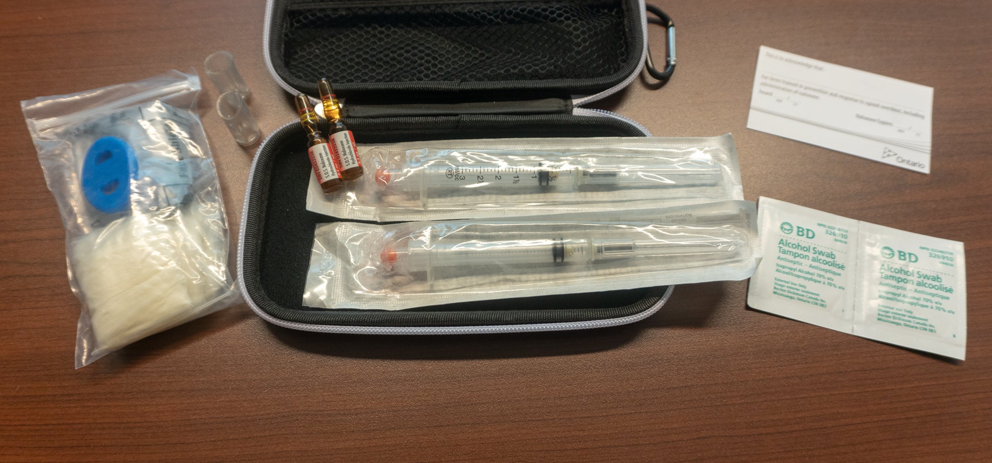 A naloxone kit with two ampules, needles, wipes, gloves and a mouth piece.