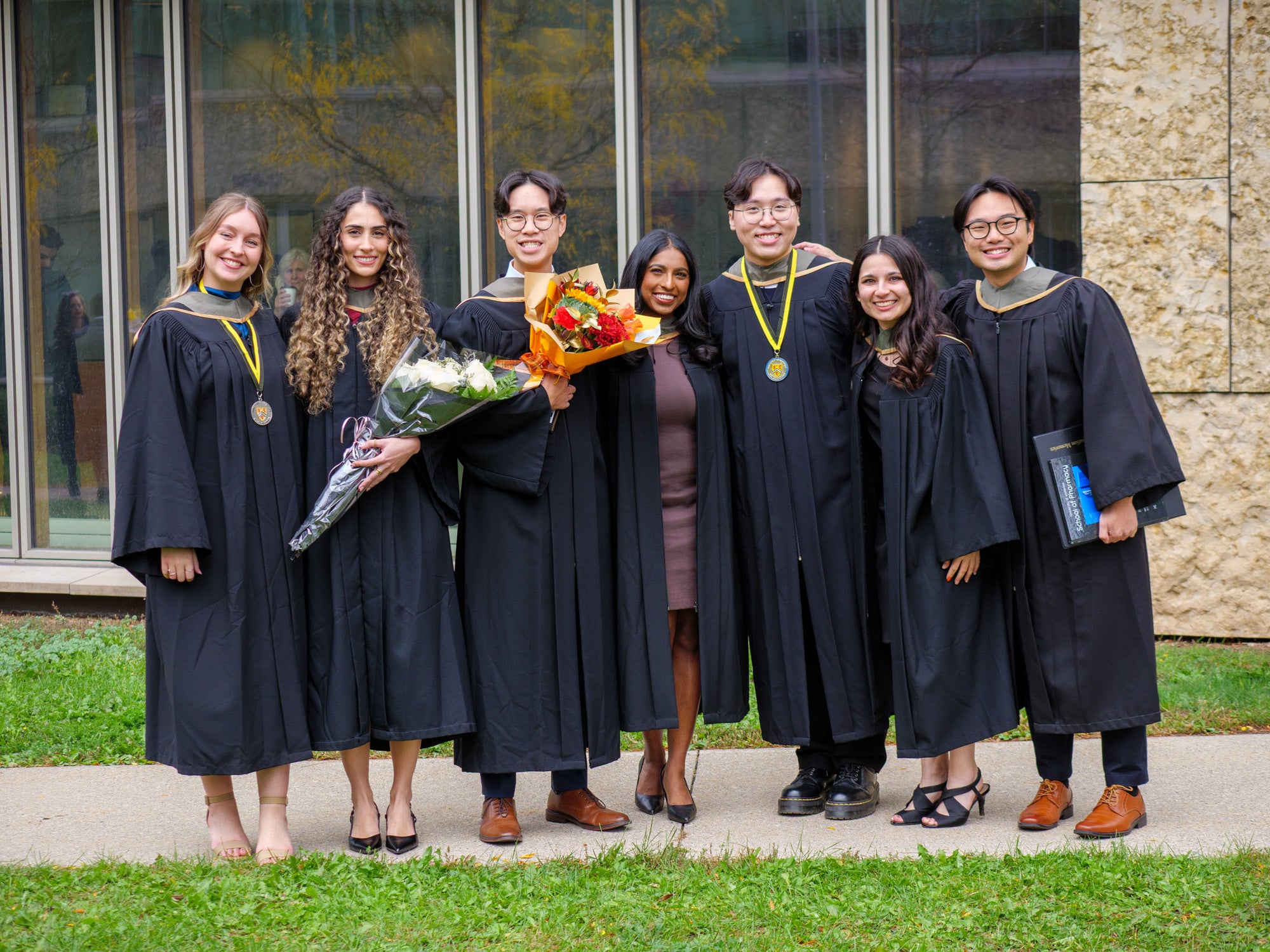 A group of graduates smiling with flowers in their robes