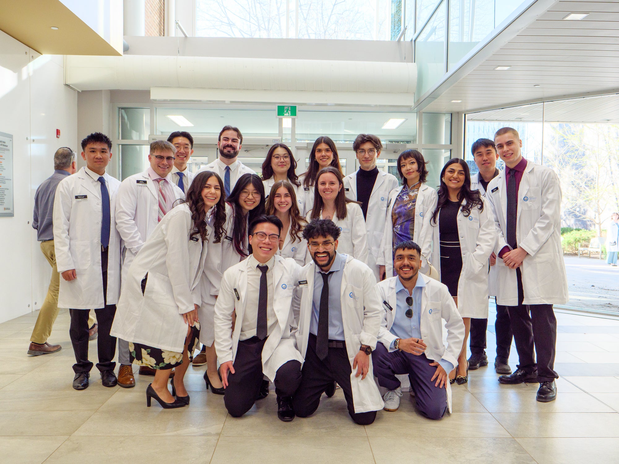 Small group of pharmacy students in white coats posing together in a bright campus lobby.