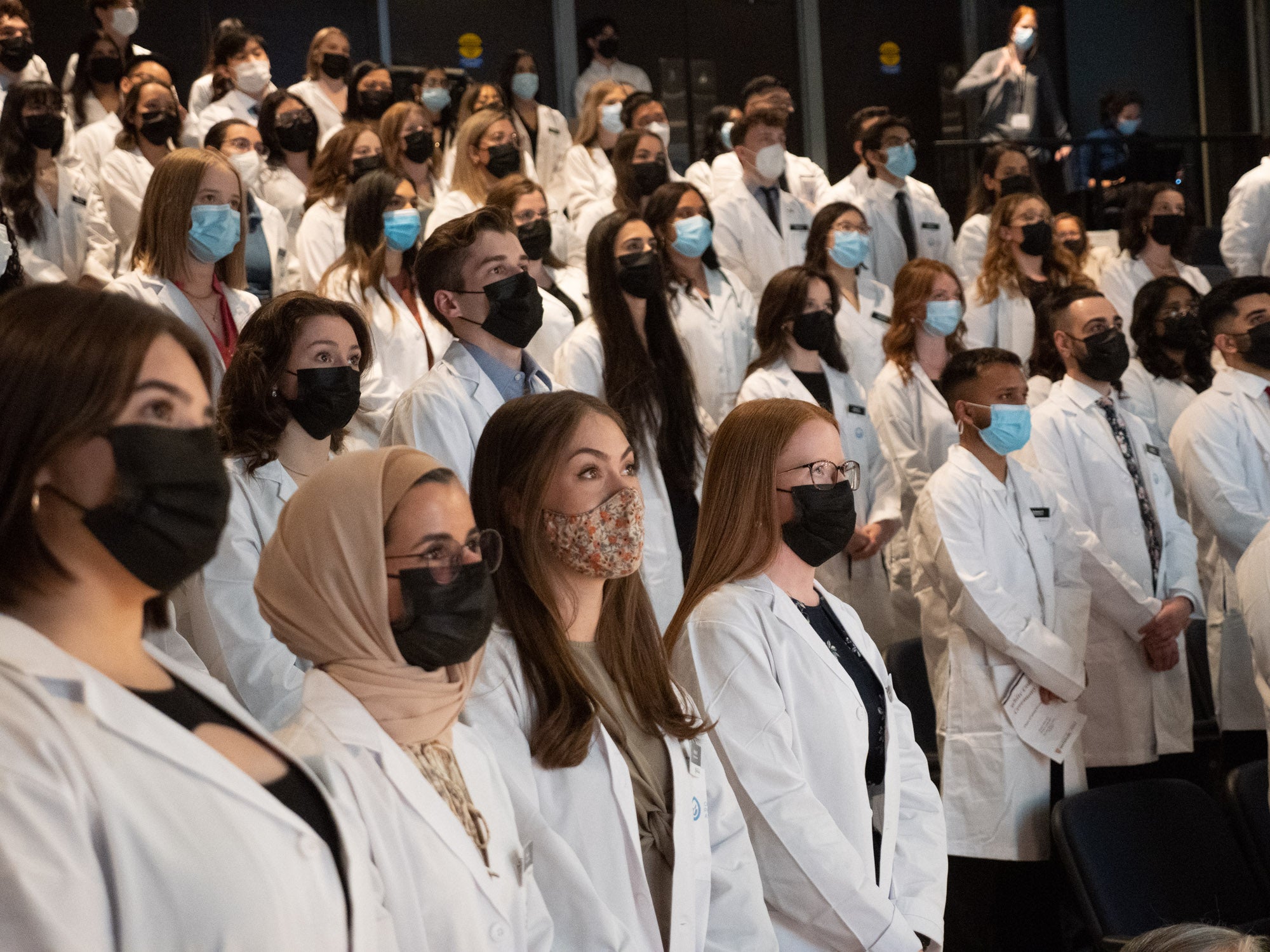 Students wearing masks and lab coats in a theatre