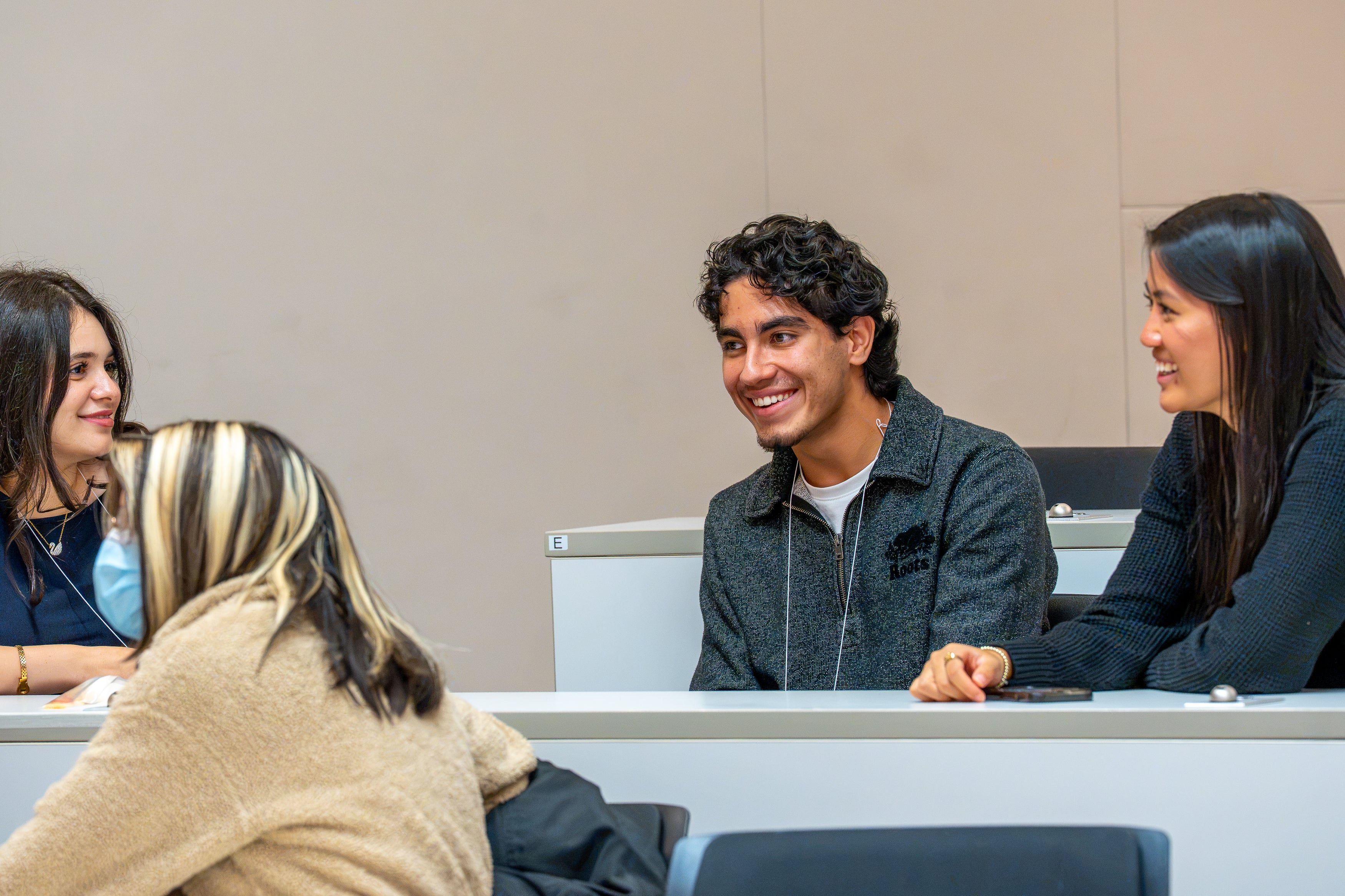 A group of attendees wearing name badges gather near two people in white lab coats in a University of Waterloo building, with a floral wall display and University of Waterloo crest in the background.