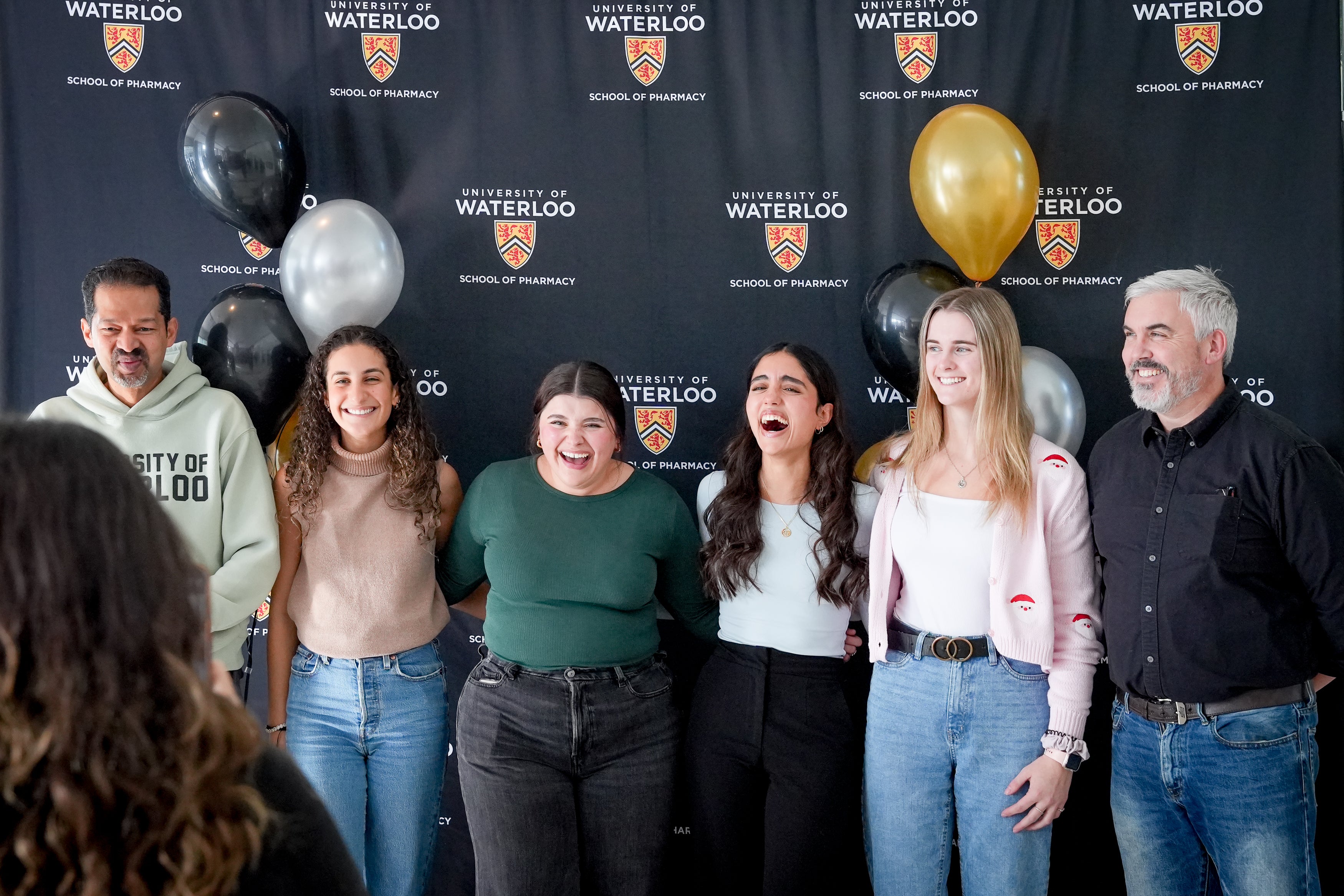 A group of students and professors laughing and smiling in front of a banner