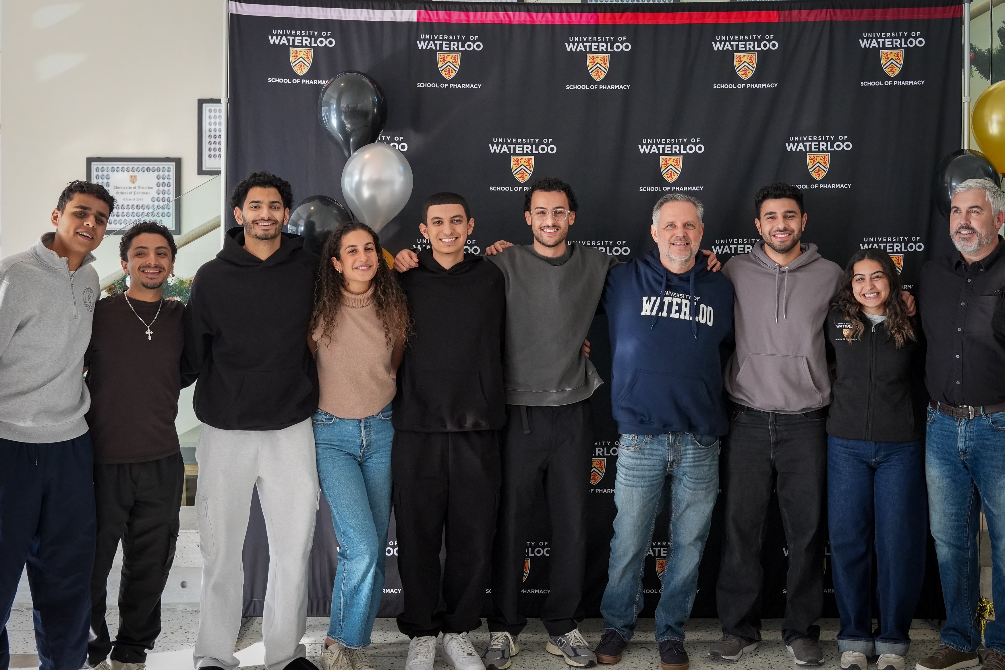A group of students smiling with their professors in front of a banner