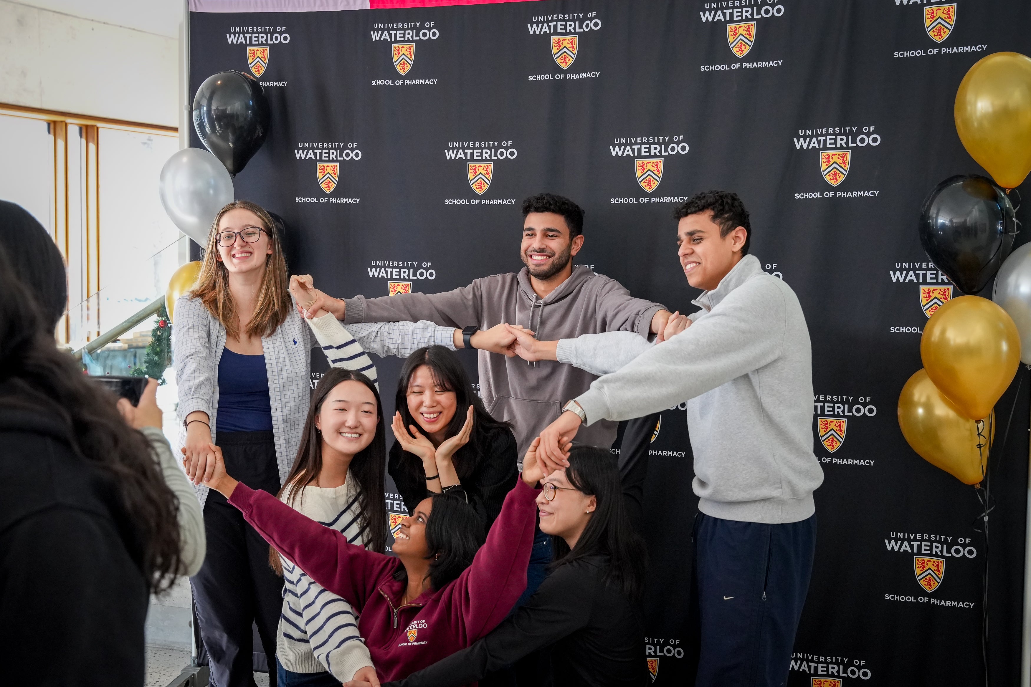 A group of students holding hands and smiling in front of a banner