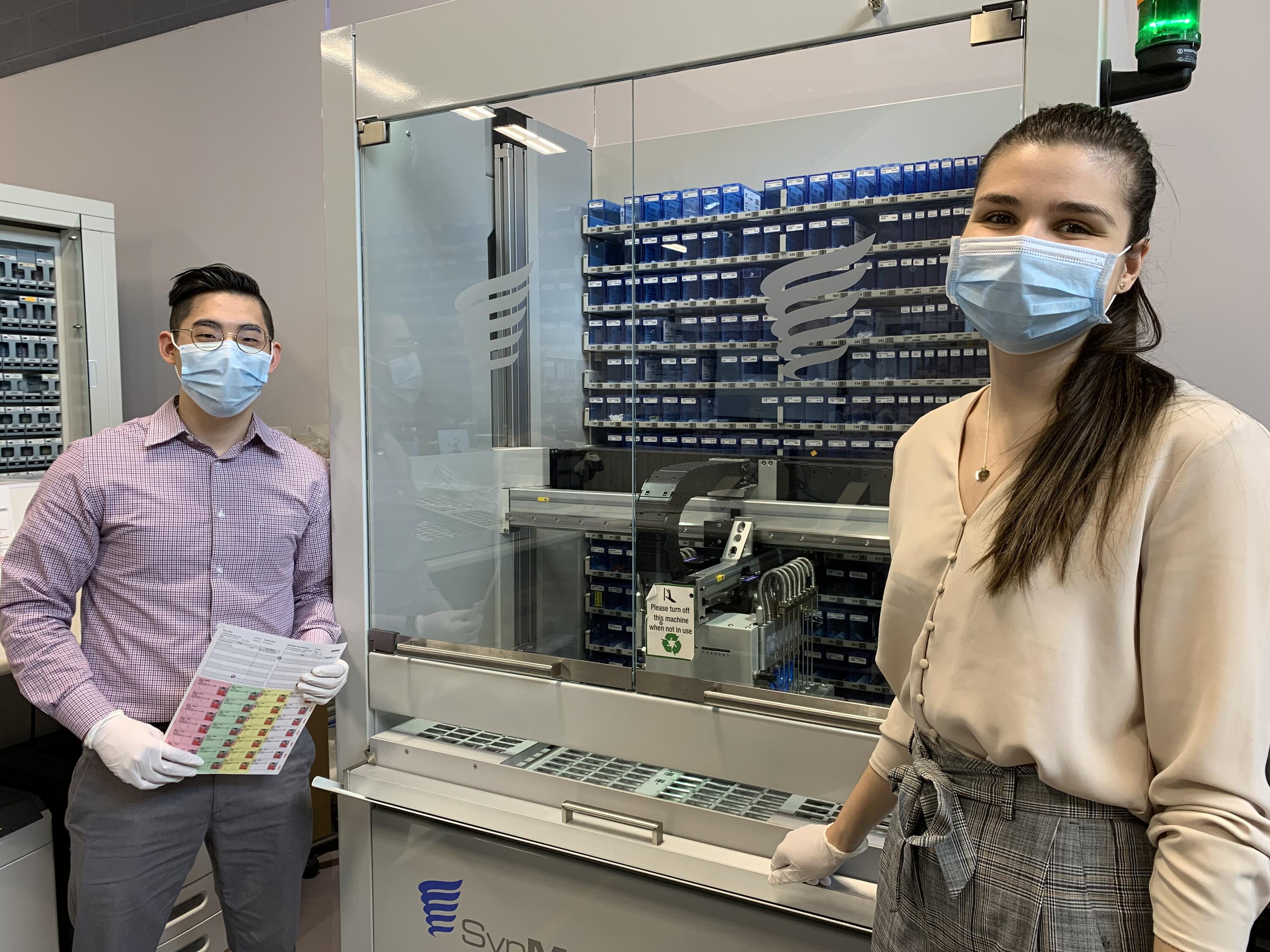 Sean Chih stands with his preceptor Jessica Kozlowski at a medication packaging machine, SynMED, in the Seamless Care Pharmacy.