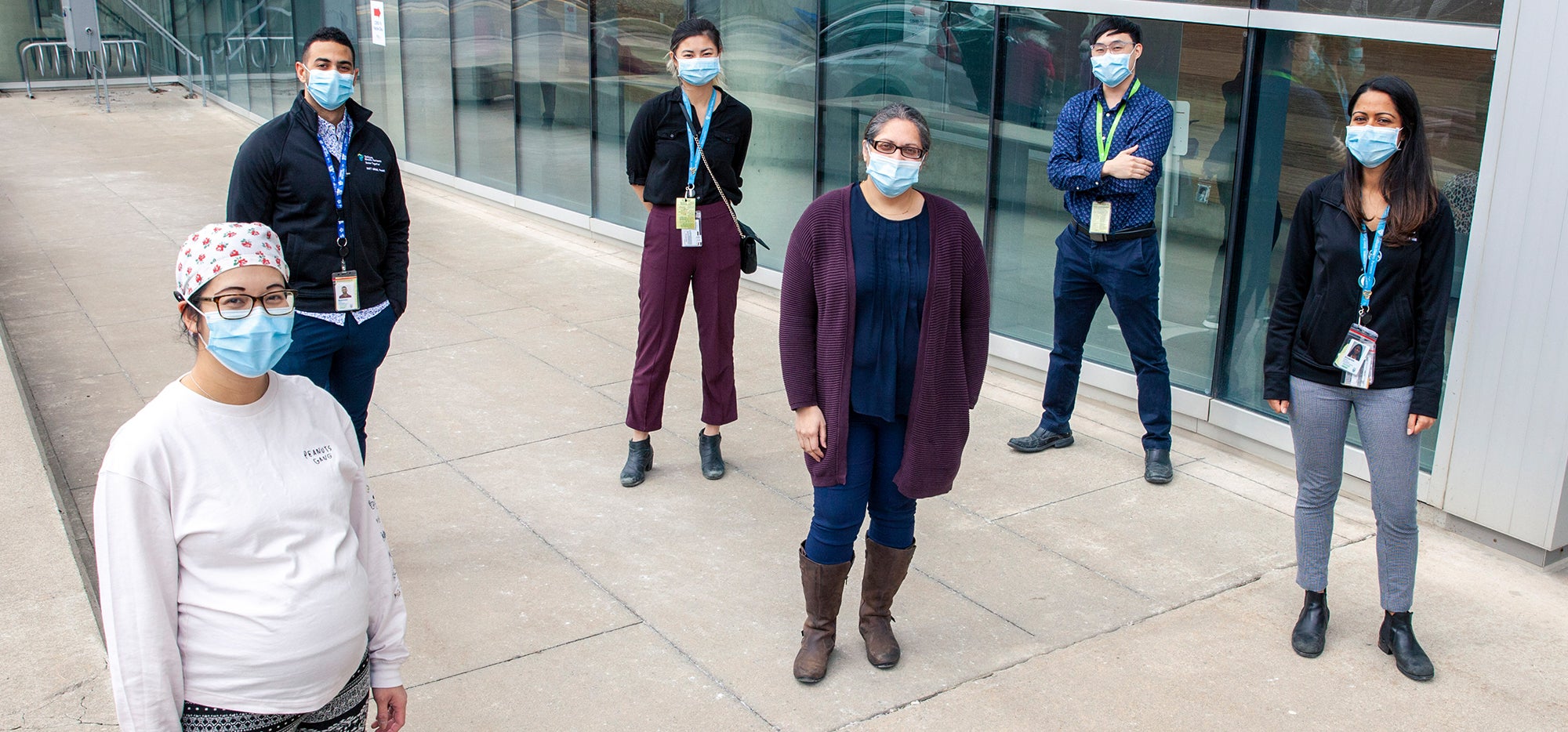 A team of healthcare providers wearing masks and socially distanced outside a hospital